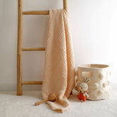 Cream 4-ply muslin baby blanket hanging on wooden ladder with toys beside it